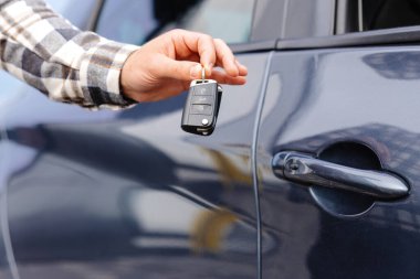 Duygusal adam elinde anahtarı tutuyor ve kameraya gülümsüyor. Yeni elektrikli arabasının anahtarını gösteren bir adam. Galeride araba alan genç bir adam..