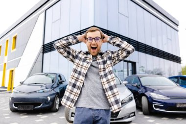 Genç bir adam çok etkileyici ve mutlu, yeni arabasının önünde duruyor..