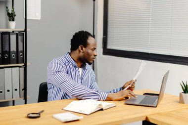 Masada oturan adam elinde kağıt tutuyor..