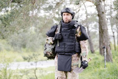 Üniformalı ve taktik yelekli genç asker ormanda çalışıyor ve geçici bir orman üssünde harekete geçmeye hazırlanıyor. Bir adam bölgeyi mayınlardan arındırmak için çalışır..