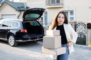 Genç bir iş kadını bir araba bagajından paketler alıyor, arabayla eve geliyor..