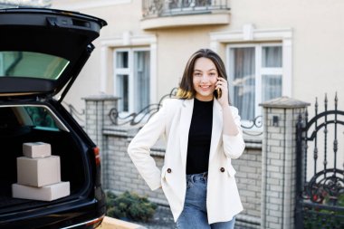 Genç iş kadını elinde paketlerle arabada duruyor, arabayla eve geliyor. Kız arabanın yanında duruyor ve konuşuyor..