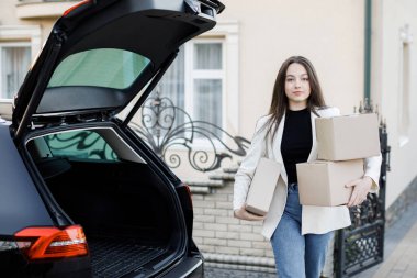 Genç bir iş kadını bir araba bagajından paketler alıyor, arabayla eve geliyor.