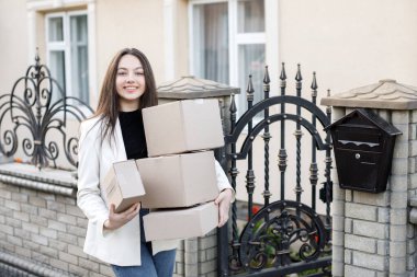 Elinde bir yığın karton kutuyla eve paket taşıyan genç bir kadın..