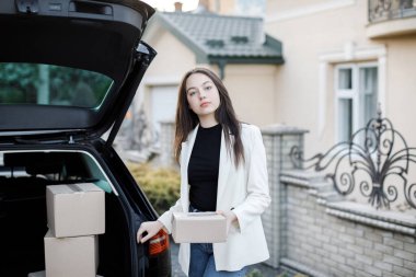Genç bir iş kadını bir araba bagajından paketler alıyor, arabayla eve geliyor..