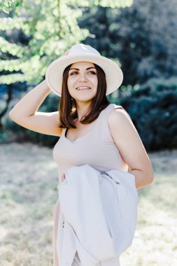 Beyaz, kendine güvenen, takım elbiseli, parkta yürüyen iş kadınının vücut portresi. Şık takım elbiseli ve beyaz şapkalı güzel bir kadın parktaki ağacın yanında duruyor.