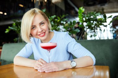 Kafede kokkuyruk içen çekici genç bir kadının portresi.