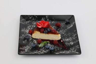 Böğürtlenli ve soslu leziz cheesecake, beyaz arka planda siyah bir tabakta..