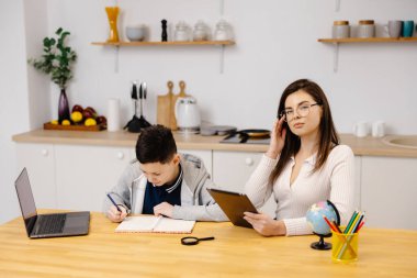 Genç bir kadın bir çocuğa tablet ve küre kullanarak derslerinde yardım ediyor. Evde eğitim gören bir öğrenci ödevini özel öğretmenin yardımıyla yapar..