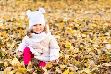 Güzel bir kız sonbahar yapraklarının ortasında parkta koşuyor ve gülümsüyor.