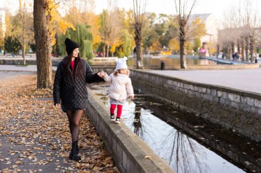 Sonbahar yürüyüşünde mutlu bir aile. Anne ve kızı parkta yürüyorlar ve güzel sonbahar doğasının tadını çıkarıyorlar.