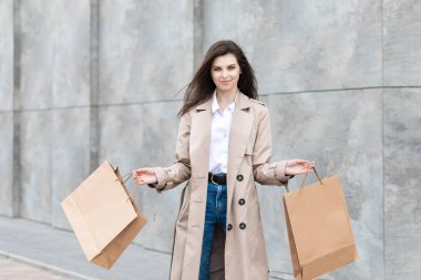 Alışveriş merkezinin yakınındaki alışveriş poşetleriyle sıradan kıyafetler içinde bir kız size paketini, tüketim satışını ve insanların konseptini sunuyor..