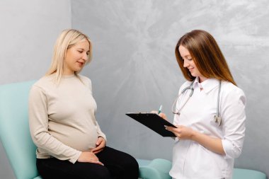 Jinekolog, jinekoloji muayenehanesinde genç bir kadın hastayla konuşuyor ve hastanın tıbbi kayıtlarına giriş yapıyor..