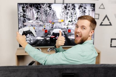 Genç adam evde vakit geçiriyor, kanepede oturuyor ve konsolda video oyunları oynuyor. Oyun oynamak ve kazanmak için joystick kullanan başarılı bir erkek.