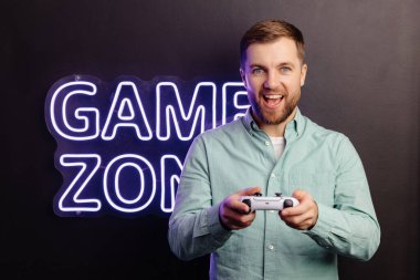 Genç sakallı adam odanın duvarında duruyor ve oynuyor, elinde kablosuz kumanda, çığlık atıyor ve yoğun bir video oyunu maçı kazanıyor.