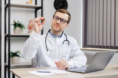 Genç, çekici bir doktor, ofisteki işyerinde oturuyor ve elinde bir kulak hortumu tutuyor..