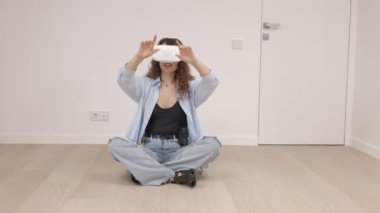 VR gözlüklü genç bir kadın modern teknolojiyi kullanarak oda tasarımı yapıyor, ellerini havada hareket ettiriyor, yenileme sırasında yeni bir dairede duruyor. Sanal gerçeklik ve onarım kavramı
