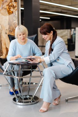 İki profesyonel kadın, takım çalışmasının ve üretkenliğin vurgulandığı çağdaş bir ofis içinde ortak bir tartışmaya girişiyor. Görüntü, iletişim ve işbirliği odaklı bir iş toplantısını vurguluyor.
