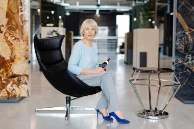 Kendine güvenen bir iş kadını modern bir ofis ortamında elinde tabletle şık bir kıyafet giyer. Kurulum profesyonelliği ve çağdaş iş estetiğini yayıyor.