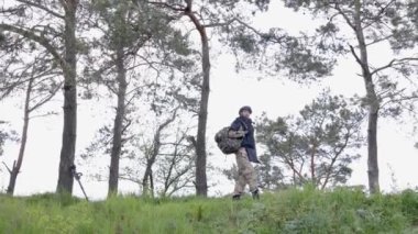 Üniformalı ve taktik yelekli genç asker ormanda çalışıyor ve geçici bir orman üssünde harekete geçmeye hazırlanıyor. Bir adam bölgeyi mayınlardan arındırmak için çalışır.