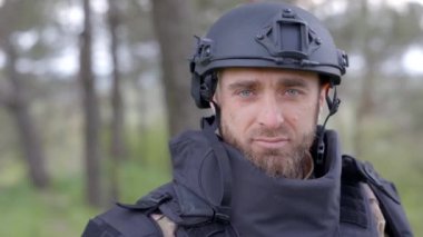 Üniformalı ve taktik yelekli genç asker ormanda çalışıyor ve geçici bir orman üssünde harekete geçmeye hazırlanıyor. Bir adam bölgeyi mayınlardan arındırmak için çalışır.