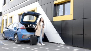Genç bir kız elektrikli arabasını şarj etmek için durdu ve bu arada bir bavul taşıyarak dinlenmeye gitti.