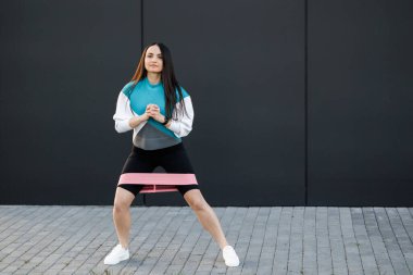 Esnek lastik direnç bantlı kadın eğitimi şehrin dışında, arka planda, karanlık duvarda.