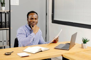 Masada oturan adam elinde kağıt tutuyor..