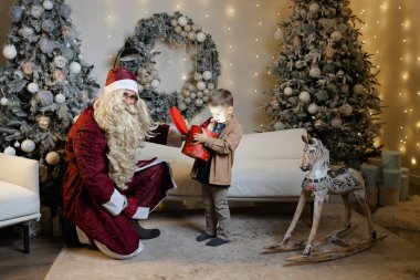 Noel Baba, Noel için dekore edilmiş bir odada bir çocuğa Noel hediyesi veriyor.