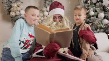 Noel Baba rahat bir kanepede otururken çocukları masal kitabıyla eğlendiriyor.
