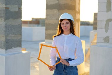 Confident female architect holding a folding ruler while inspecting a building under construction at sunset clipart