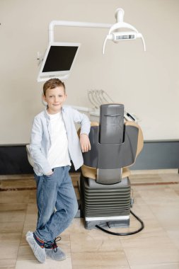 Diş muayenesinden sonra dişçide otururken kameraya gülümseyen mutlu çocuk..