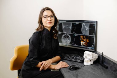 Diş hekimi hastaya çenesinin röntgenini gösterir. Dişçinin ekranında panoramik diş görüntüsü var..