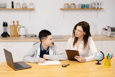 Genç bir kadın bir çocuğa tablet ve küre kullanarak derslerinde yardım ediyor. Evde eğitim gören bir öğrenci ödevini özel öğretmenin yardımıyla yapar..