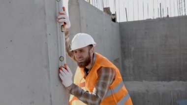 İnşaatçı-tamirci, ustabaşı, koruyucu bir miğferle beton bir binanın merdivenlerini kontrol eder.