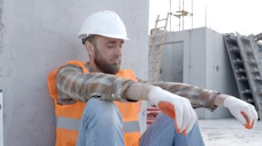 Tamirci, miğfer ve yelek giyen ustabaşı iş yerinde alet çantası ve cetvelin yanındaki binada dinlenmek için oturuyor.