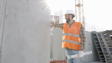 İnşaatçı, miğfer ve yelek giyen ustabaşı inşaat halindeki bir binada iş yerinde çalışıyor.