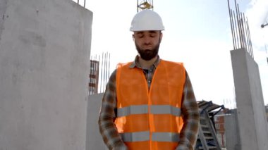 Tamirci, koruyucu miğfer ve yelek giyen ustabaşı inşaat alanında duruyor ve cetveli elinde tutuyor.
