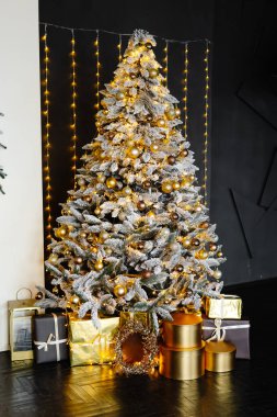 Altın ve gümüş mücevherlerle süslenmiş Noel ağacı ve altında bir sürü hediye kutusu olan iplik ışıkları, bayram atmosferi.