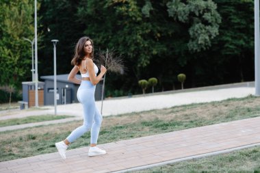 Güneşli bir yaz gününde şehir parkında koşan sağlıklı bir kadın fiziksel aktivite yoluyla sağlıklı bir yaşam tarzını teşvik ediyor.