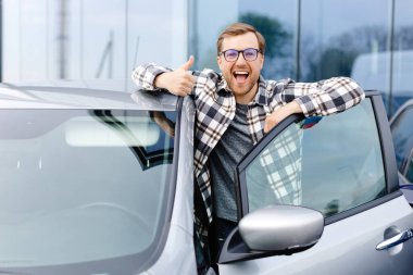 Otomobilin yanında duran neşeli adam, galeri merkezinde araba alırken işaret veriyor.