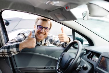 Genç adam yeni arabasının camından bakıyor, modern galeriden almadan önce kontrol ediyor. Galeride araba alan ya da kiralayan neşeli adam..