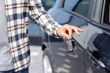 Duygusal adam elinde anahtarı tutuyor ve kameraya gülümsüyor. Yeni elektrikli arabasının anahtarını gösteren bir adam. Galeride araba alan genç bir adam..