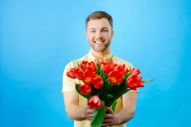 Elinde canlı kırmızı lale buketi tutan bir adam, tarafsız bir zemine karşı çiçeklerin güzelliğini sergiliyor..
