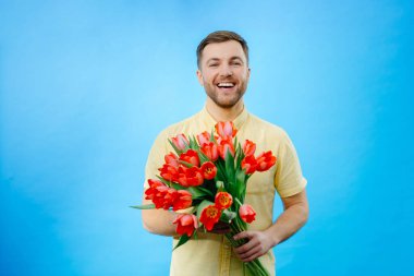 Elinde canlı kırmızı lale buketi tutan bir adam, tarafsız bir zemine karşı çiçeklerin güzelliğini sergiliyor..