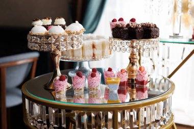 Çeşitli hamur işleri ve pastalar taze böğürtlenlerle süslenmiş cam ve altın katlı sergiler düğün resepsiyonunda