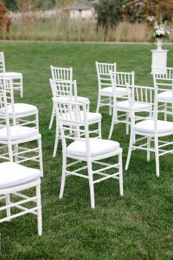 Yeşil çimlere dizilmiş zarif beyaz yastıklı sandalyeler açık hava düğün töreni için sofistike bir ortam yaratır.