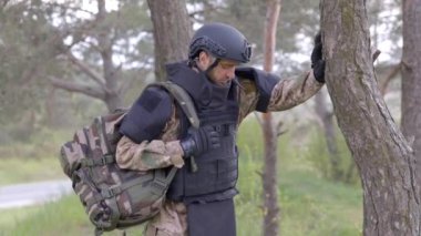 Üniformalı ve taktik yelekli genç asker ormanda çalışıyor ve geçici bir orman üssünde harekete geçmeye hazırlanıyor. Bir adam bölgeyi mayınlardan arındırmak için çalışır.