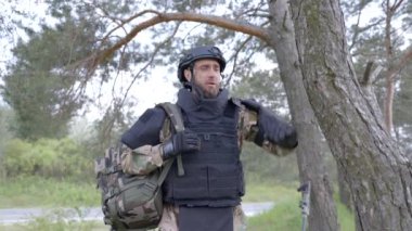 Üniformalı ve taktik yelekli genç asker ormanda çalışıyor ve geçici bir orman üssünde harekete geçmeye hazırlanıyor. Bir adam bölgeyi mayınlardan arındırmak için çalışır.