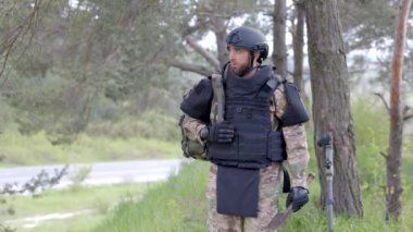 Üniformalı ve taktik yelekli genç asker ormanda çalışıyor ve geçici bir orman üssünde harekete geçmeye hazırlanıyor. Bir adam bölgeyi mayınlardan arındırmak için çalışır.